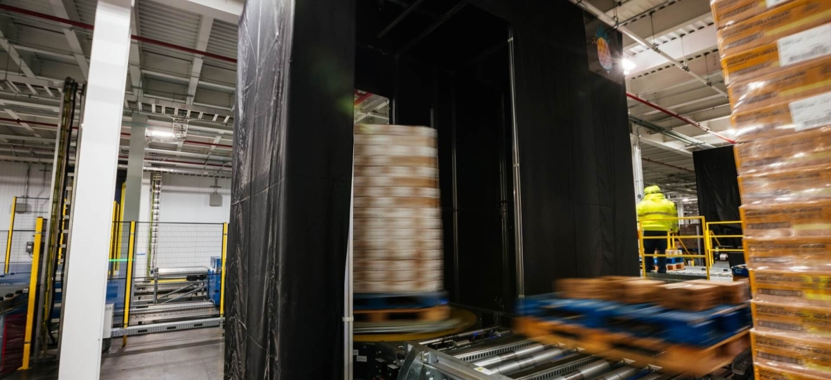 A neatly stacked pallet positioned on a Airsun Express Eye conveyor system in a clean, well-organized, automated cold storage warehouse, with safety guardrails and scanning stations in the vicinity.