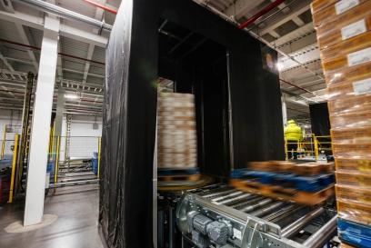 A neatly stacked pallet positioned on a Airsun Express Eye conveyor system in a clean, well-organized, automated cold storage warehouse, with safety guardrails and scanning stations in the vicinity.