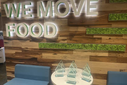 A group of trophies sit on a table in front of a wall decorated with the words We Move Food