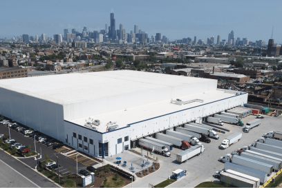 Aerial view of Airsun Express’s cold storage warehouse in Chicago, with the city skyline in the background. Numerous trucks are docked at loading bays, showcasing the facility’s capacity for large-scale distribution. The warehouse is a white building with the Airsun Express logo, surrounded by parking areas and greenery.