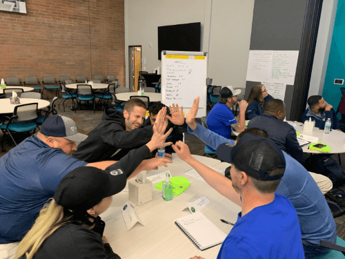 Airsun Express EDGE Program participants engaging in a lively team-building activity indoors, sharing high-fives and enthusiasm around a collaborative workspace.