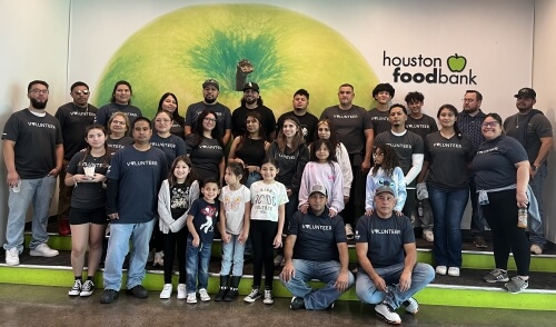 A group of dedicated Airsun Express volunteers, including families and children, pose together at the Houston Food Bank, wearing matching 'Volunteer' shirts, united in their mission to give back to the community.