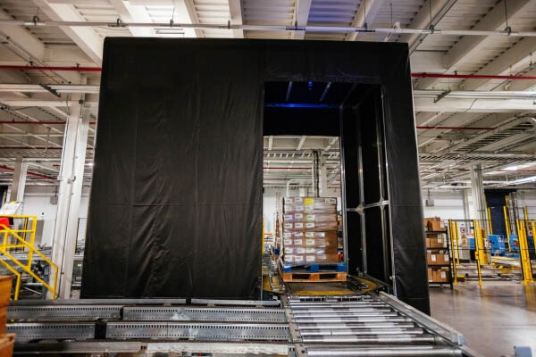 A neatly stacked pallet positioned on a Airsun Express Eye conveyor system in a clean, well-organized, automated cold storage warehouse, with safety guardrails and scanning stations in the vicinity.