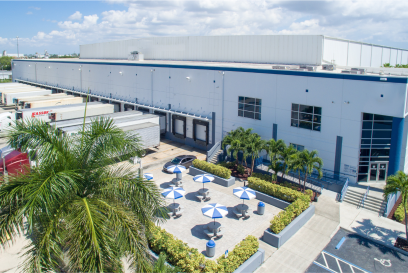 Aerial view of Airsun Express Logistics cold storage facility in Miami showcasing the expansive warehouse, loading docks with trucks, and the landscaped outdoor area with shaded seating.