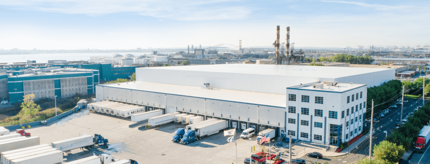 A large Airsun Express cold storage warehouse in New Jersey, with the Airsun Express logo, featuring multiple loading docks with trucks, located in an industrial area with proximity to a port.