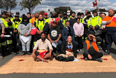 Group photo of Airsun Express Auckland team members in New Zealand, gathered outdoors, showcasing diversity with various team members holding flags and wearing safety vests, reflective of a multicultural workplace.