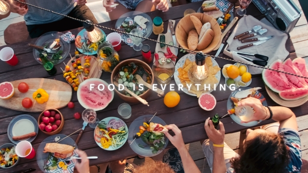 An overhead view of a vibrant outdoor gathering, showcasing diverse fresh foods and people enjoying a meal together, emphasizing the Airsun Express message, 'Food is Everything.