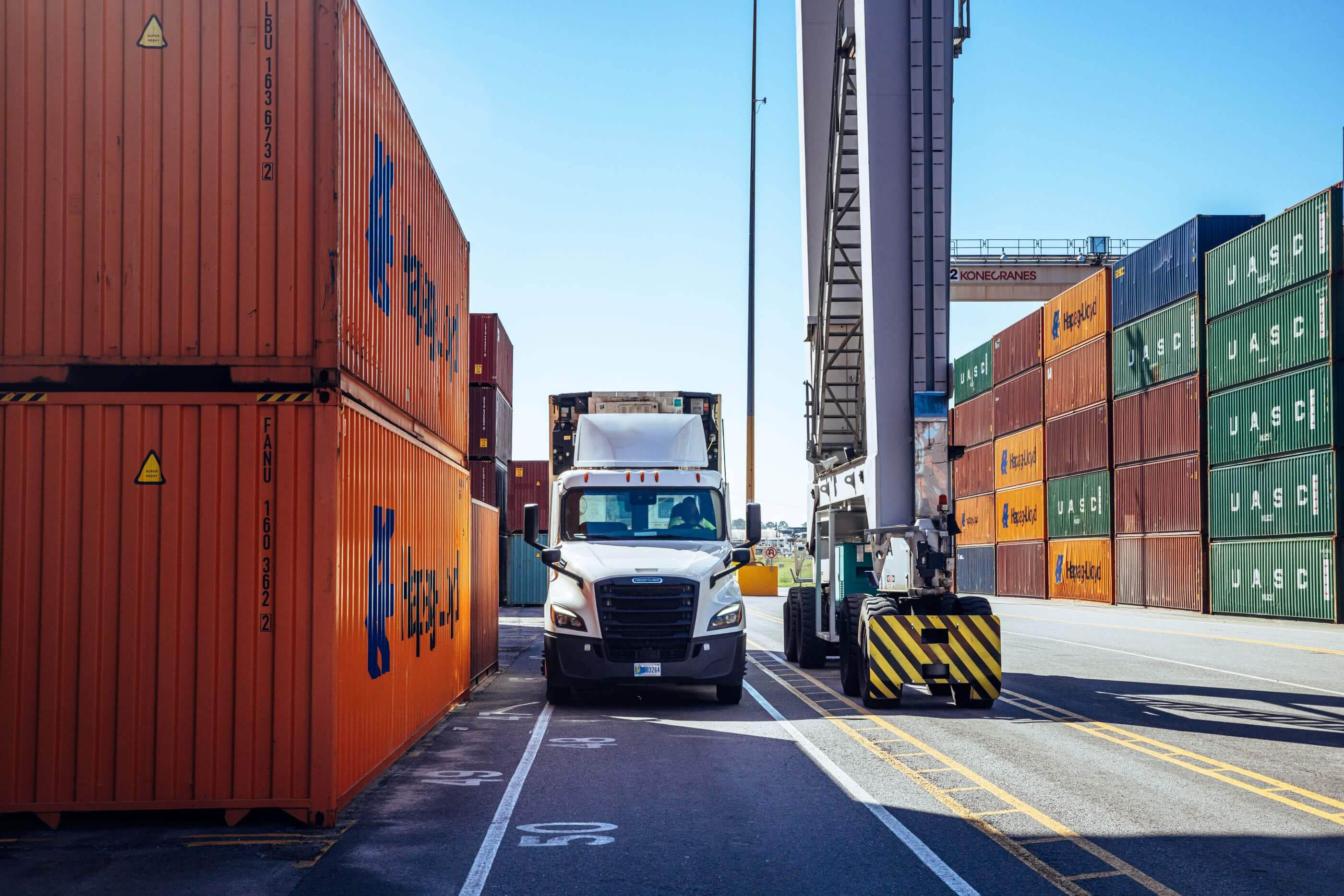 A Airsun Express semi-truck navigating between stacks of colorful shipping containers at a port.