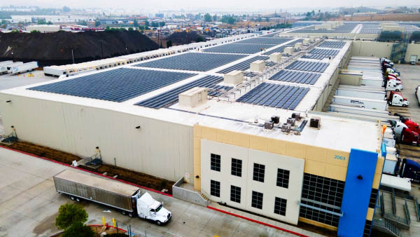 An aerial view of a Airsun Express cold storage facility featuring rooftop solar panels and a fleet of trucks ready for transportation services.